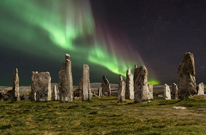 The Northern Lights lighting up the sky above a circle of standing stones.
