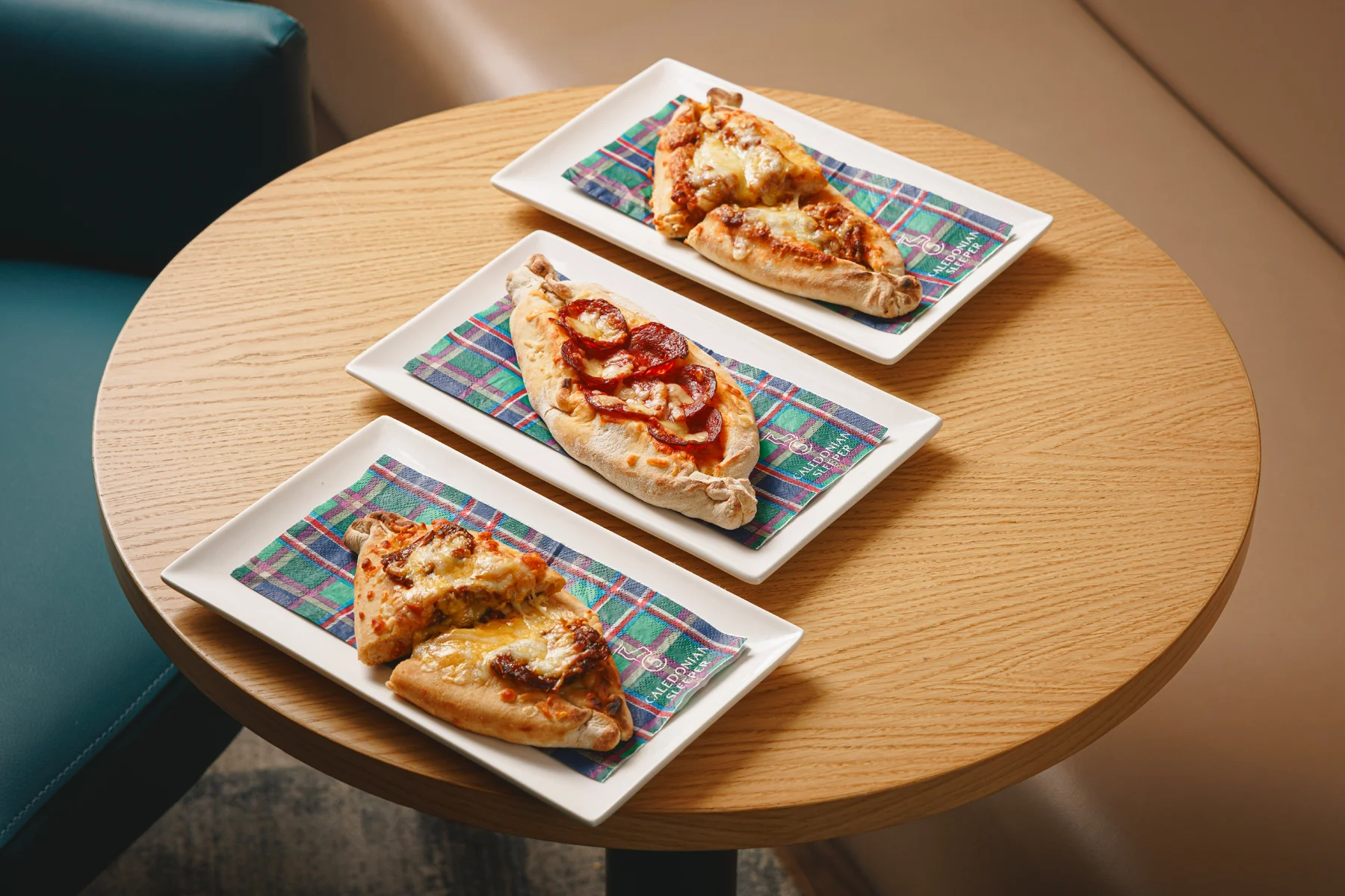 Three plates of pizzas, all slices are sitting on a Caledonian Sleeper tartan napkin. 