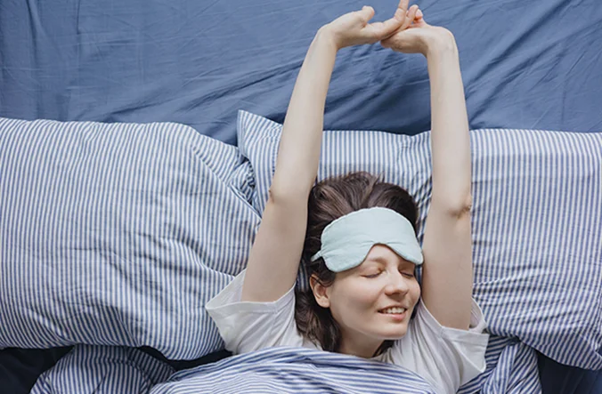 Woman stretching in bed with eye mask on.