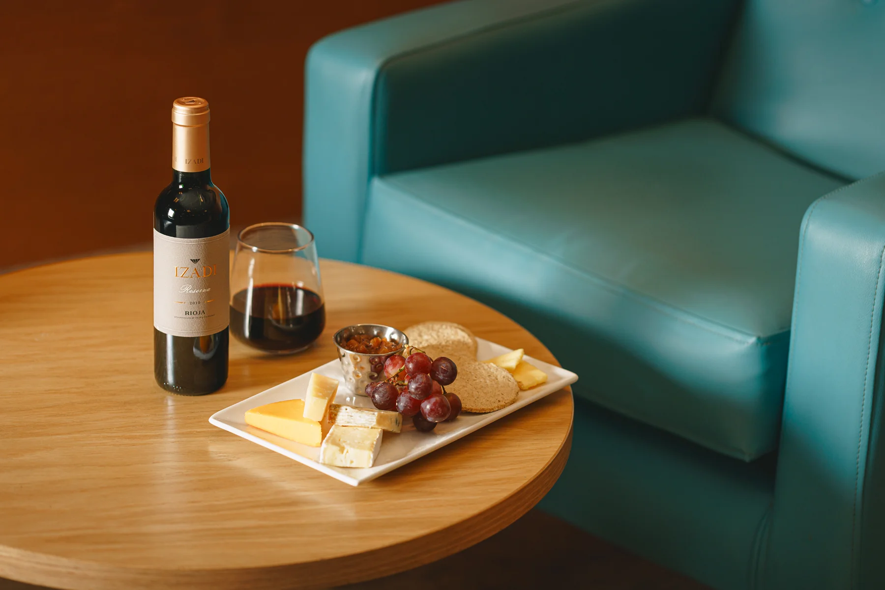 Bottle and glass of red wine with a cheeseboard. 