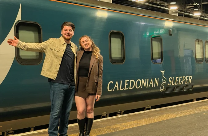 A male and female couple standing in front of the Caledonian Sleeper train.