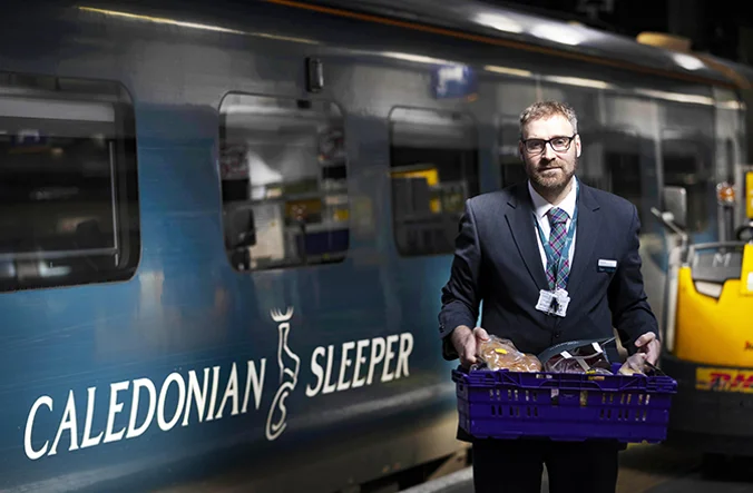 Caledonian Sleeper representative standing on platform by a train.
