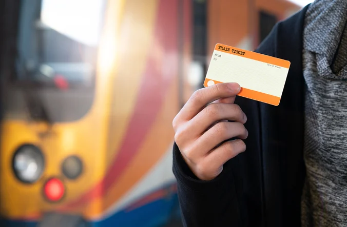 Person holding train ticket in front of train