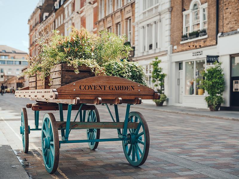 'Covent Garden" area name sign on a wooden cart with flowers on a street in Covent Garden, London, UK, on a bright summer day. Selective focus.